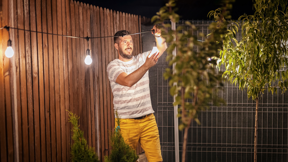 Un homme orne le jardin de guirlandes lumineuses pour ambiancer l'espace.